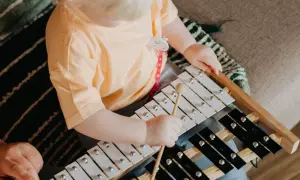 Małe dziecko z blond włosami bawi się cymbałkami, tworząc pierwsze melodie. Zastanawiasz się, co zagrać na cymbałkach?