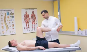 Fizjoterapeuta bada pacjenta z podejrzeniem naderwanego ścięgna. Na ścianie wiszą anatomiczne plakaty.