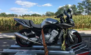 Srebrny motocykl Yamaha Fazer na przyczepce, gotowy do przerejestrowania. W tle pole kukurydzy i błękitne niebo.