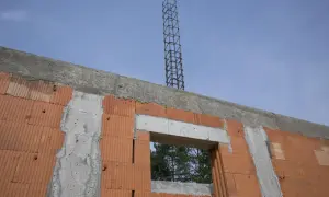 Budowa domu, widoczny fragment ściany z pustaków ceramicznych, betonowy nadproże okna i zbrojenie słupa. Wieniec opuszczony, czekający na dalsze prace.