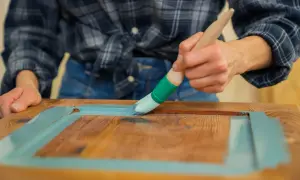 Person streicht mit Pinsel und hellblauer Farbe über Holz. Ein DIY-Projekt, um alten Möbeln neuen Glanz zu verleihen. Lack auf Lack streichen.