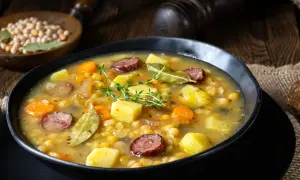 Gęsta grochówka z kawałkami ziemniaków, marchewki, boczku i kiełbasy, udekorowana gałązką tymianku.