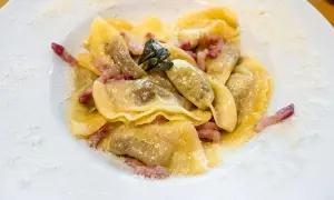 Casoncelli alla bergamasca, pasta ripiena con pancetta e salvia, spolverati di parmigiano su un piatto bianco.
