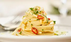 Ein Berg Spaghetti Aglio e Olio, garniert mit frischer Petersilie und scharfen Chilischeiben, auf einem Teller.
