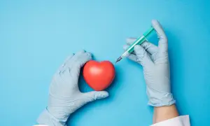 Mains gantées tenant un cœur rouge et une seringue, évoquant une intervention comme une coronarographie.