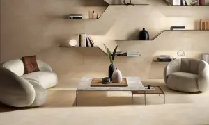 Ein modernes Wohnzimmer in warmen Beigetönen. Ein geschwungenes Sofa und ein Sessel laden zum Entspannen ein. Regale mit Büchern und Deko schmücken die Wand.