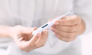 Hände halten ein digitales Thermometer, das die Temperatur für den Eisprung anzeigt.