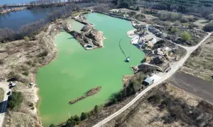Widok z lotu ptaka na turkusowe jezioro zajączkowskie, otoczone piaskowymi skarpami i zielenią. Widać sprzęt wydobywczy i łódź.