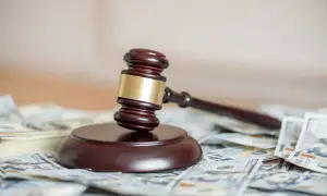 Młotek sędziowski na stosie banknotów dolarowych. Zastanawiasz się, ile kosztuje sprawa o podwyższenie alimentów?