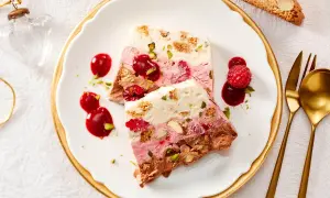 Gefrorener Kuchen mit Beeren, Nüssen und Schokolade auf einem Teller mit Sauce und Löffel.