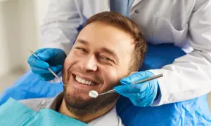 Uśmiechnięty mężczyzna u dentysty. Badanie stomatologiczne, które może pomóc rozwiać wątpliwości dotyczące implantów zębowych a nowotworów.