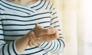Frau hält ihren Daumen, der schmerzt, als ob sie einen Schnappfinger Daumen hätte.
