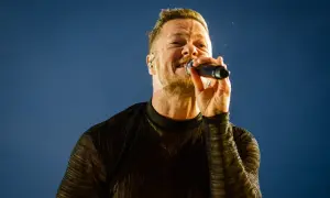 Wokalista Imagine Dragons śpiewa do mikrofonu na tle błękitnego nieba.