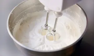 Schlagobers wird mit einem Handmixer in einer Edelstahlschüssel aufgeschlagen. Die cremige Masse ist bereit für süße Köstlichkeiten.