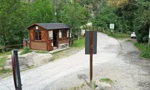 Caseta de información y señalización para senderismo en Aigüestortes. Un camino de grava y asfalto se adentra en un bosque frondoso.