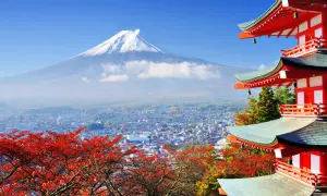 Malownicze widoki Japonii: góra Fudżi w chmurach, miasto i czerwone liście klonu obok czerwonej pagody.