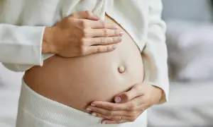 Dłonie kobiety obejmują ciążowy brzuch, wyczekując momentu, kiedy czuć ruchy dziecka.