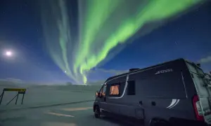 Ein Wohnmobil steht unter dem faszinierenden Himmel, wo grüne **polarlichter** tanzen. Mond und Sterne leuchten über der verschneiten Landschaft.
