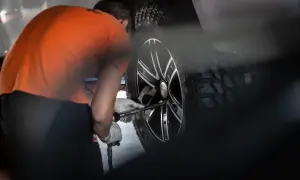Mechanik w pomarańczowej koszulce dokręca śruby w kole, przygotowując **trójkąt opony** do dalszej jazdy.