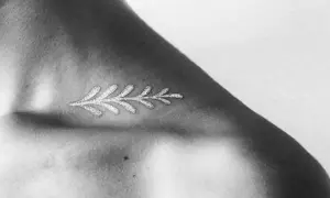 Delicado diseño de rama con **tatuajes blancos en piel negra**, resaltando la delicadeza y el contraste en el hombro.