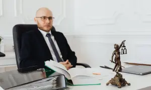 Prawnik w garniturze siedzi przy biurku, obok stosu dokumentów i otwartej księgi. Zastanawiasz się, ile kosztuje notariusz?