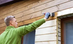 Man målar panel utomhus med en pensel. Träet är ljust och fräscht.