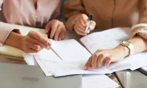 Dwie kobiety analizują dokumenty, szukając informacji, kiedy nie trzeba zgłaszać darowizny do urzędu skarbowego.