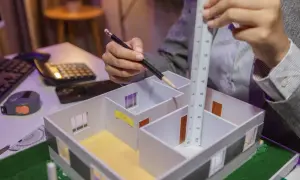 Osoba z ołówkiem i linijką mierzy model domu, ucząc się, jak obliczyć długość zastrzałów.