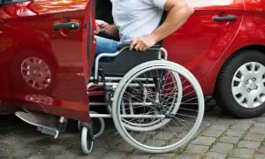 Persona in sedia a rotelle si avvicina a un'auto rossa, modello 104, per salire.
