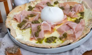 Pizza mit Burrata, Mortadella und Pesto auf einem Teller.