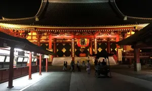 Nocny widok na świątynię Senso-ji z czerwoną latarnią i ludźmi spacerującymi po dziedzińcu.