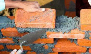 Budowa muru z cegieł, gdzie cegły wystające co druga w murze tworzą wzór. Tynkarz układa kolejną cegłę.