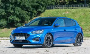 Niebieski Ford Focus 1.0 EcoBoost z czarnym dachem, zaparkowany na żwirowej nawierzchni, na tle zieleni.