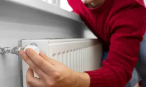 Mężczyzna w czerwonym swetrze reguluje termostat grzejnika, oszczędzając energię. To jego sposób na wykorzystanie bonu ciepłowniczego.