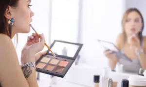 Makijażystka w pracy, nakłada pomadkę pędzelkiem. W tle druga kobieta wykonuje makijaż.