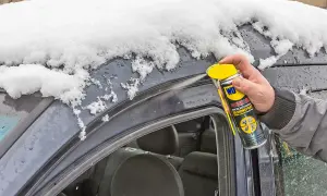 Hand sprüht Silikonspray auf die Gummidichtung des Autos, um sie vor Frost zu schützen und die Gummidichtung zu reparieren.