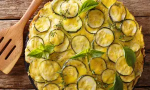 Une délicieuse scarpaccia de courgettes, garnie de basilic frais et de thym, prête à être servie avec une spatule en bois.