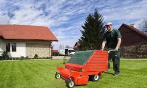 Ogrodnik z wertykulatorem na trawniku przed domem.