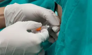 Rękawiczki medyczne trzymają igłę do punkcji lędźwiowej, która pomaga wykryć choroby OUN, infekcje i krwawienia.