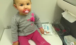 Mała dziewczynka z smoczkiem siedzi na siedzeniu w samolocie Ryanair. Obok niej leżą pieluchy i chusteczki.