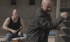 Dwóch mężczyzn, jeden gra na perkusji, drugi tańczy. To scena z teledysku zespołu Kult, który mieszka w Polsce.