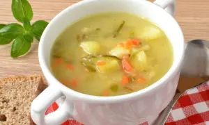 Zupa ogórkowa Ani gotuje się w białej misce, obok kromki chleba i gałązki bazylii.