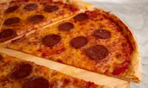 Kawałki pizzy pepperoni z roztopionym serem na desce.