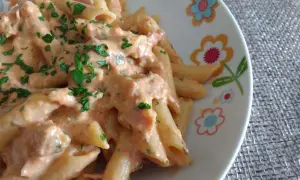 Penne al baffo cremose e gustose, condite con un sugo rosato e prezzemolo fresco, servite su un piatto decorato con fiori colorati.