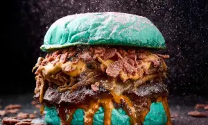 Una hamburguesa gigante con pan azul, carne jugosa, queso derretido y crujiente tocino, perfecta para un festival hamburguesa.