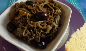 Paparine verdura in umido con olive nere, servite in una ciotola bianca su un piatto viola, accanto a una fetta di pane.