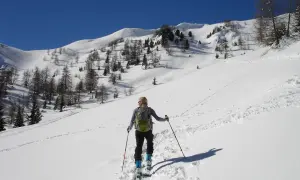 Sciatrice con zaino e bastoncini, in un paesaggio innevato con alberi radi e montagne sullo sfondo. La **forca canapine** è il suo obiettivo.