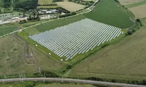 Widok z lotu ptaka na dużą farmę paneli słonecznych otoczoną polami i linią kolejową.