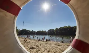 Sonniger Tag am Badesee in Hannover. Menschen planschen im Wasser und entspannen am Sandstrand, gesehen durch einen Rettungsring.