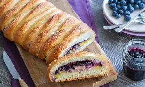Una deliziosa treccia mochena ripiena di mirtilli e crema, cosparsa di zucchero, pronta per essere gustata.